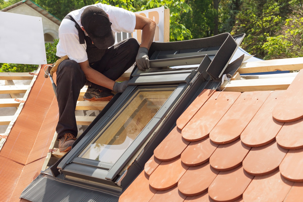 man on tiled roof installing window
