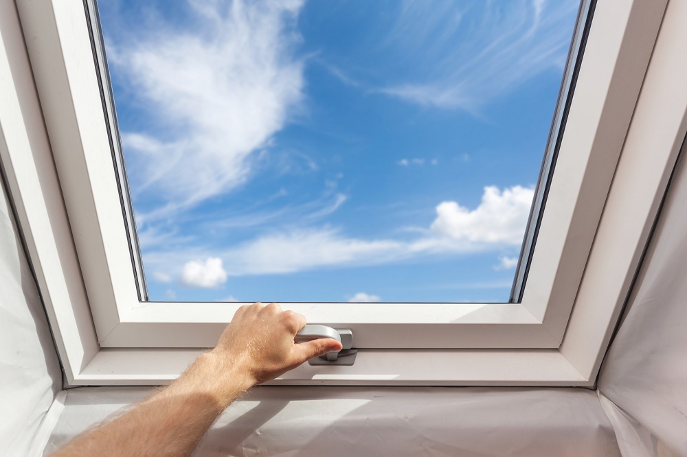 Man close new skylight (mansard window) in an attic room against blue sky